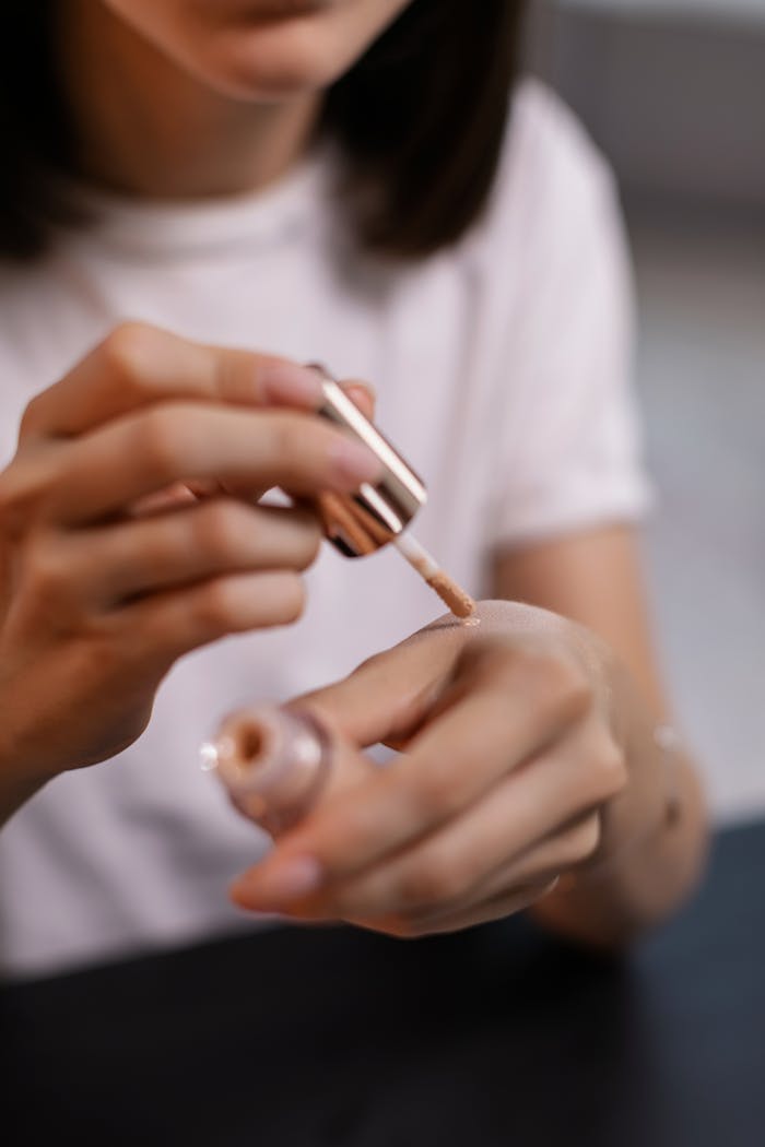 A womans hands testing liquid foundation with a cosmetic applicator indoors.