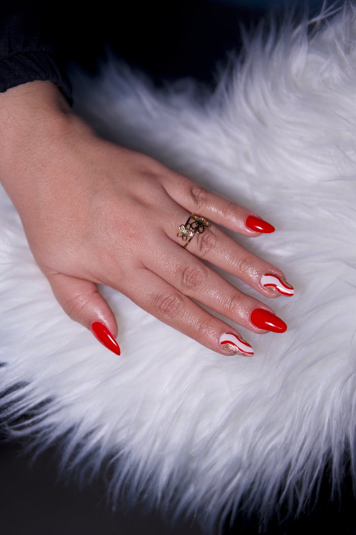 Close-up of a stylish red manicure with a gold ring on a fluffy white surface.