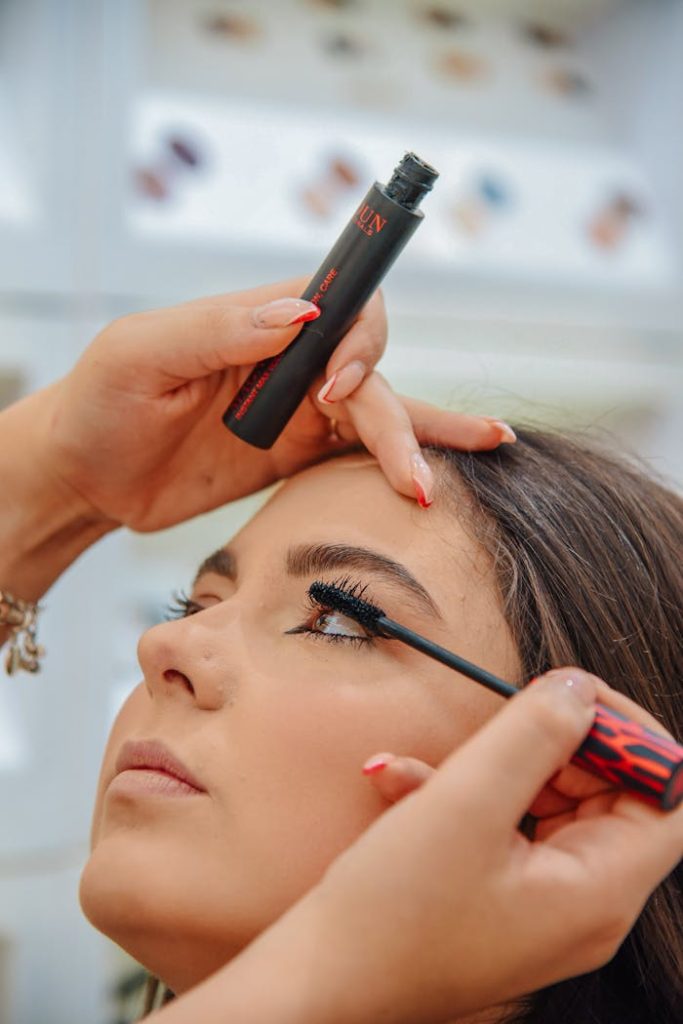 person-applying-mascara-on-woman-s-lashes-15046693 Detailed close-up of a woman applying mascara with focus on eye makeup indoors.