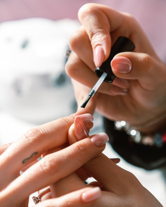woman-getting-a-manicure-16041438 Close-up of a professional manicure with nail polish application in bright lighting.